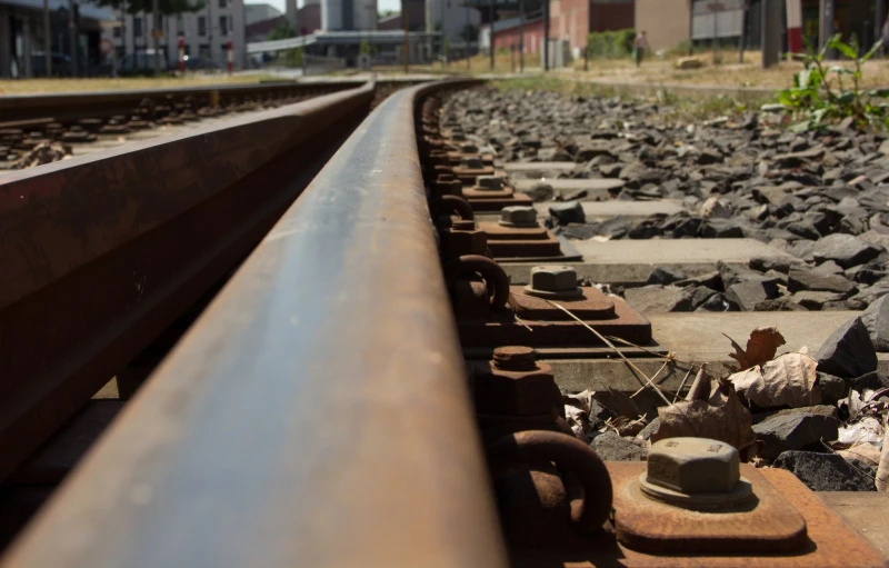 an old, rusty looking railroad line with stones and a building in the background