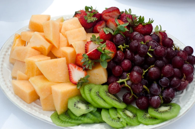 gs, melons, kiwi, cucumber, strawberries and bananas arranged on a plate