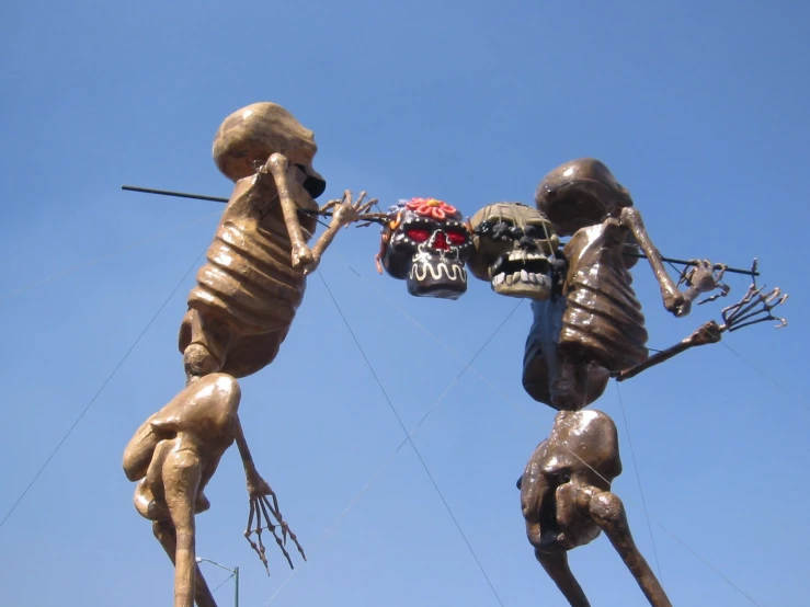 two sculptures of skeletons climbing each other against a clear blue sky