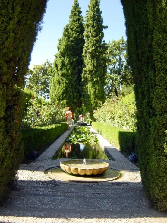 a fountain in the middle of a courtyard with trees and hedges