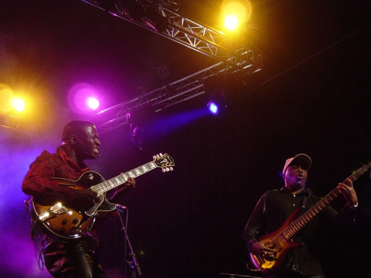 two people play the guitar while they stand in front of a band