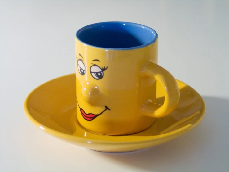 a yellow coffee mug with a smiling face in a yellow saucer