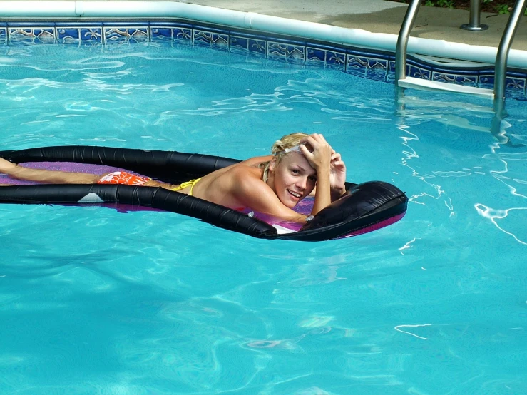 a young woman wearing a bikini sitting on a black inflatable swimming float