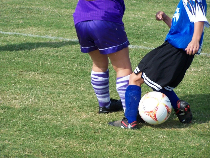 two children are kicking a soccer ball on the grass