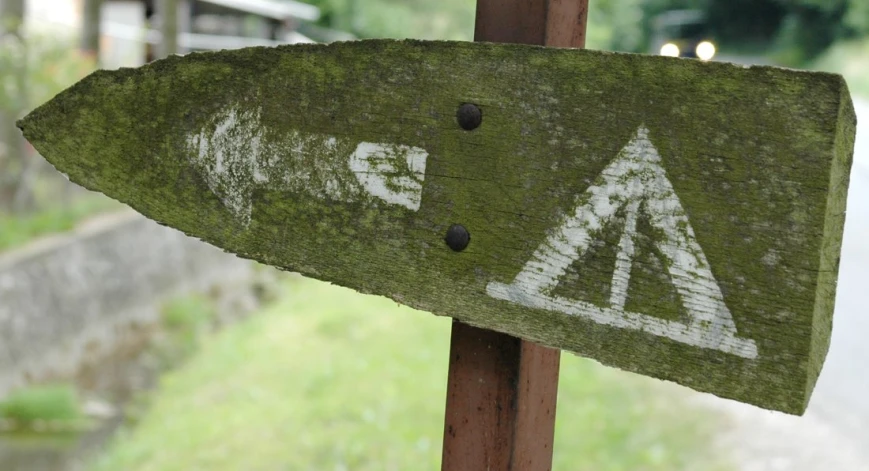 a wooden sign on a post that has a direction point and a number and arrows painted on it