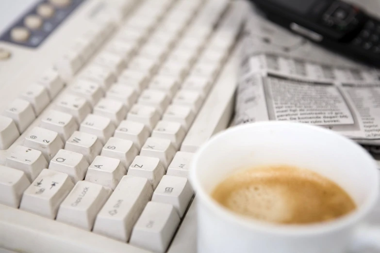 a cup with liquid sitting next to a white keyboard