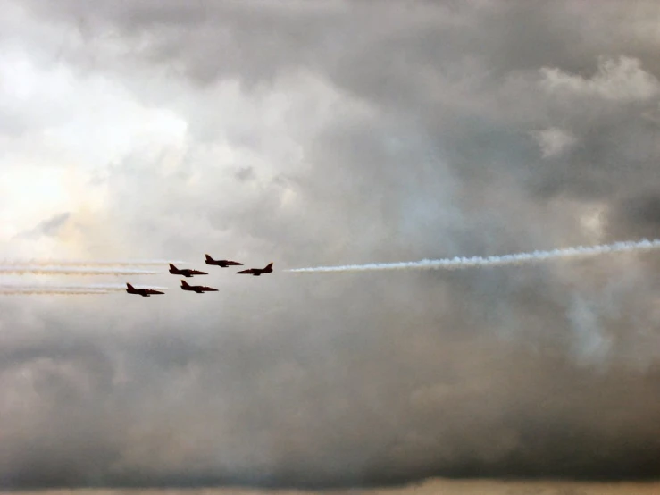 four jet planes flying through a gray cloudy sky