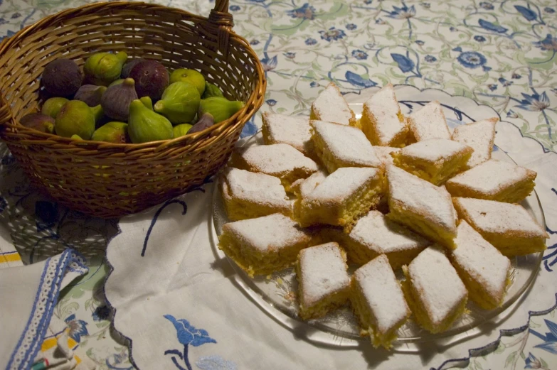 a basket of green figs sits next to a plate of small desserts