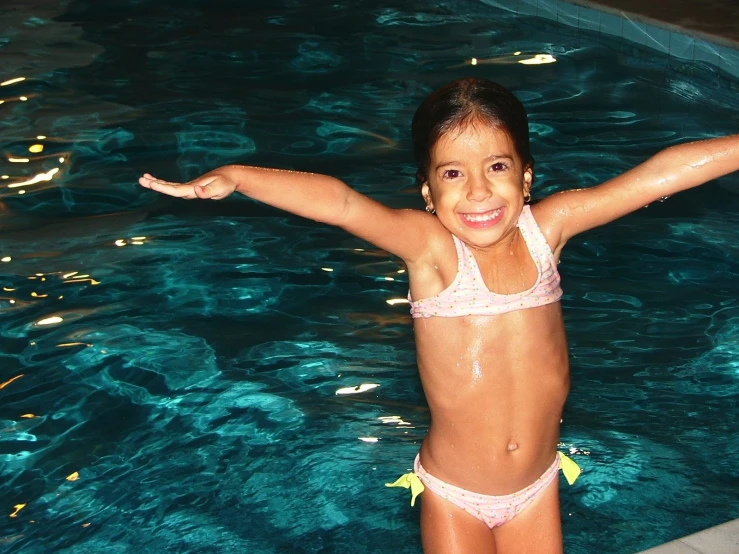a little girl standing in the water by a swimming pool