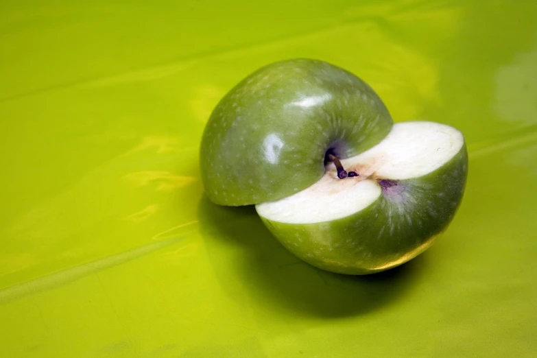 an apple with a bite missing sitting on a green surface