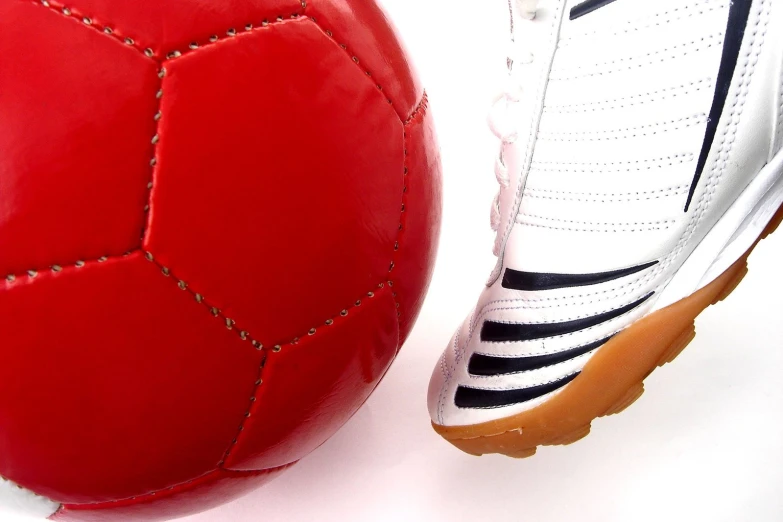 a red and white shoe standing next to a soccer ball