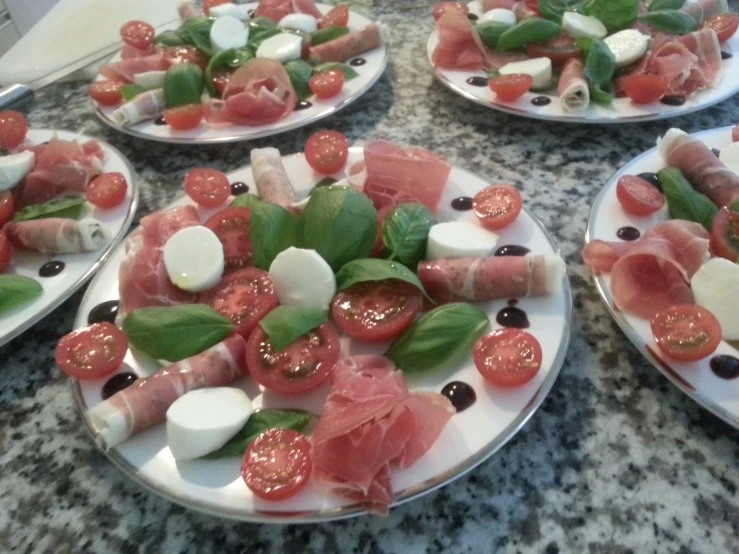 a display with many plates of appetizers that include tomatoes, cheese and sliced figs