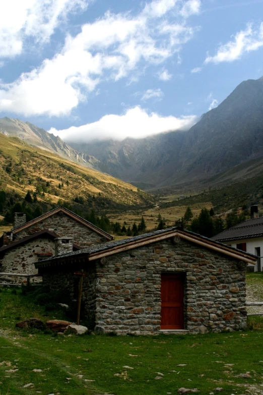 an old stone building in front of mountains with a red door