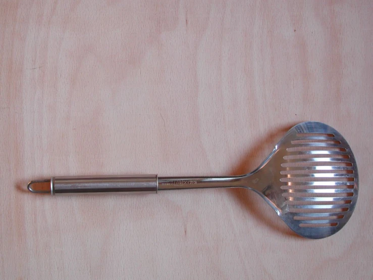 a large stainless spoon sitting on top of a wooden table