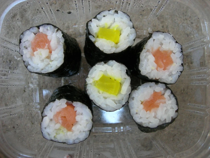 a glass bowl containing six sushi, with yellow and black pieces of sushi