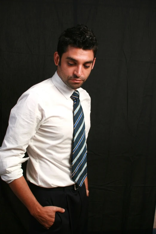 a young man standing and looking serious wearing a white shirt and blue striped tie