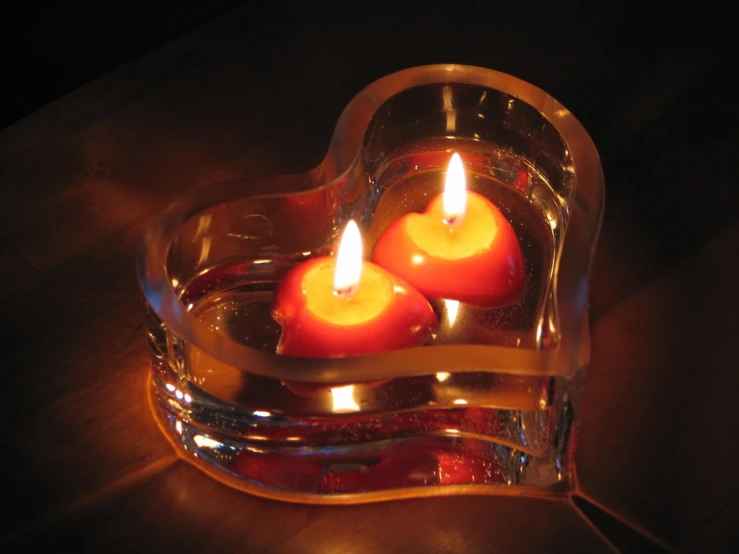 three heart shaped candles are in a clear holder
