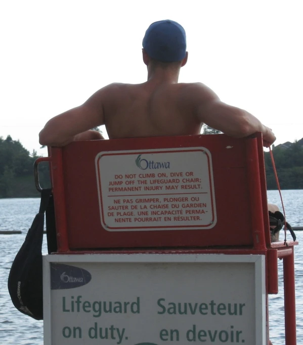 a shirtless man sitting at a red boat in front of water