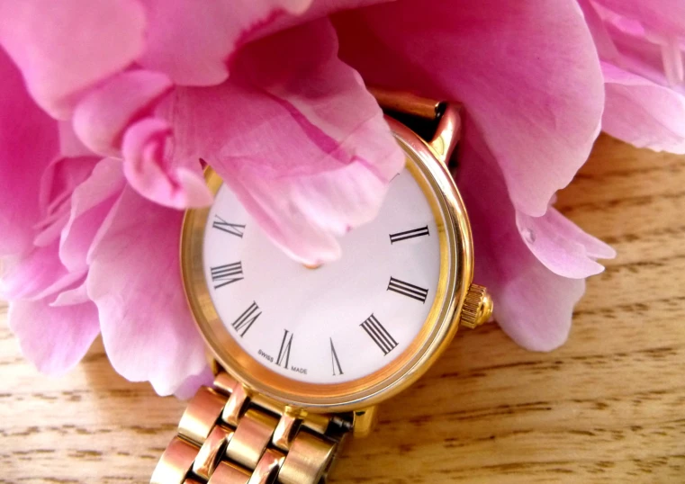 a watch sitting under pink flowers on top of a table