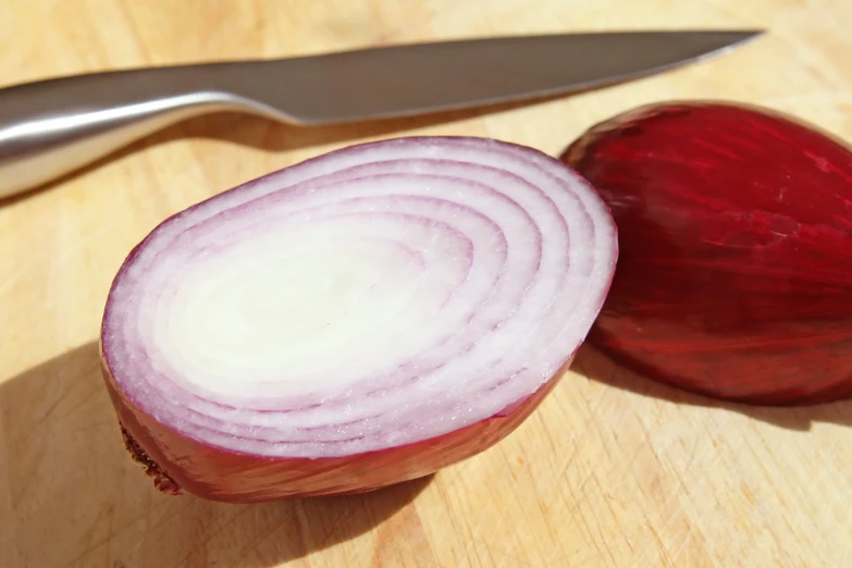 a sliced red onion next to a knife on a  board