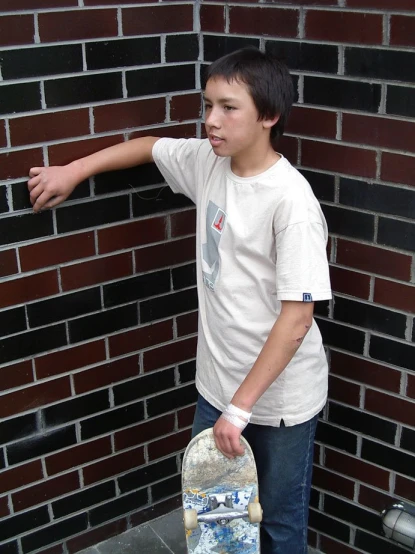 a boy leans on his skateboard as he points at a brick wall