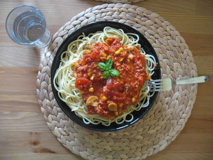 a bowl filled with spaghetti and sauce on top of a woven place mat