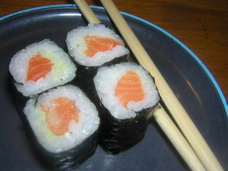 a small plate holding rolls with sushi, chopsticks