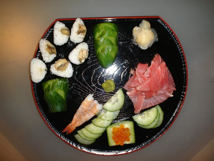 a black plate topped with sushi and cucumbers