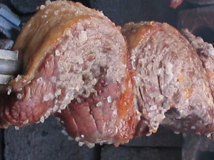 meat being cooked on a grill with tongs