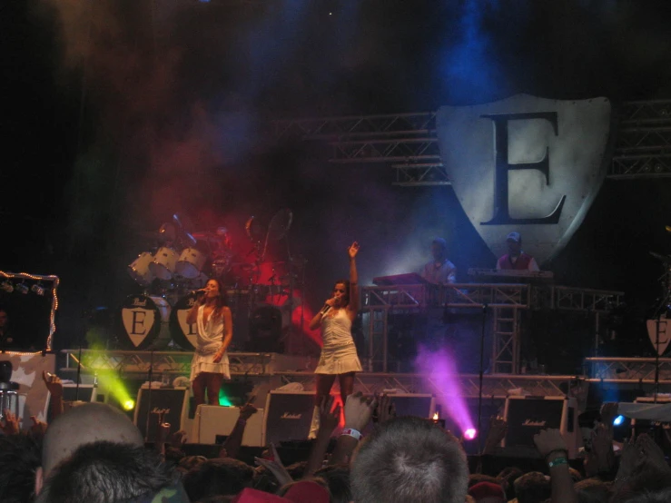 three women are on stage singing with purple and red lighting