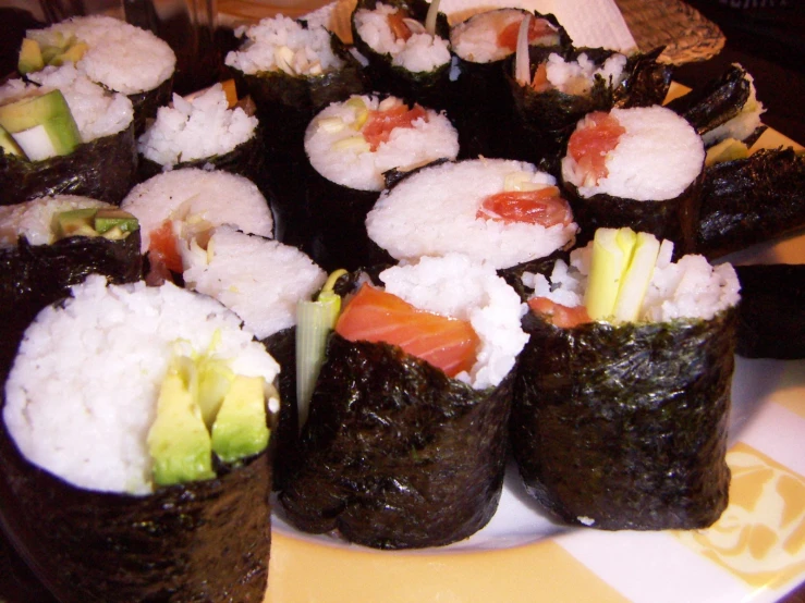 sushi rolls with salmon and avocado are piled high in rows