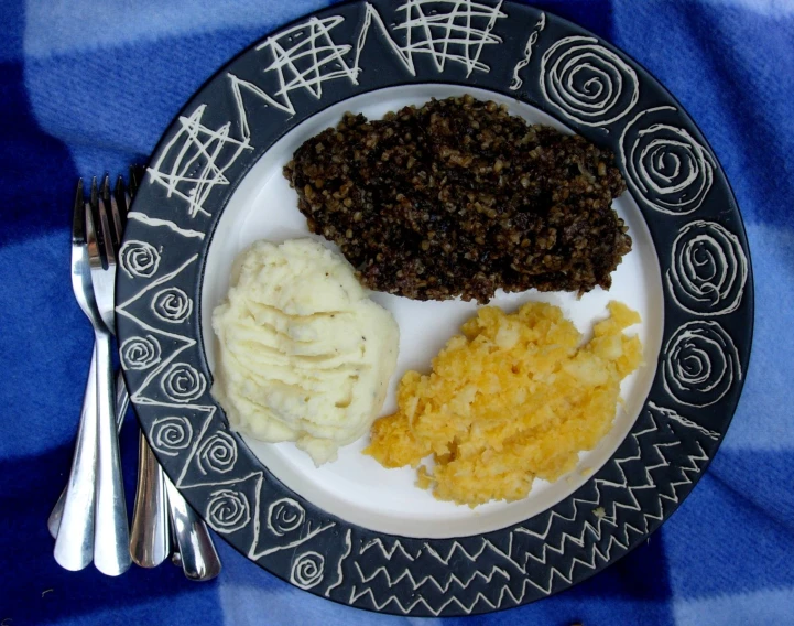 a plate with a black and white design holding rice, beans and mashed potatoes