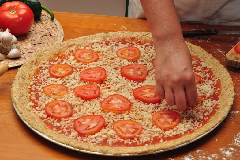 someone sprinkleing tomatoes on top of a pizza