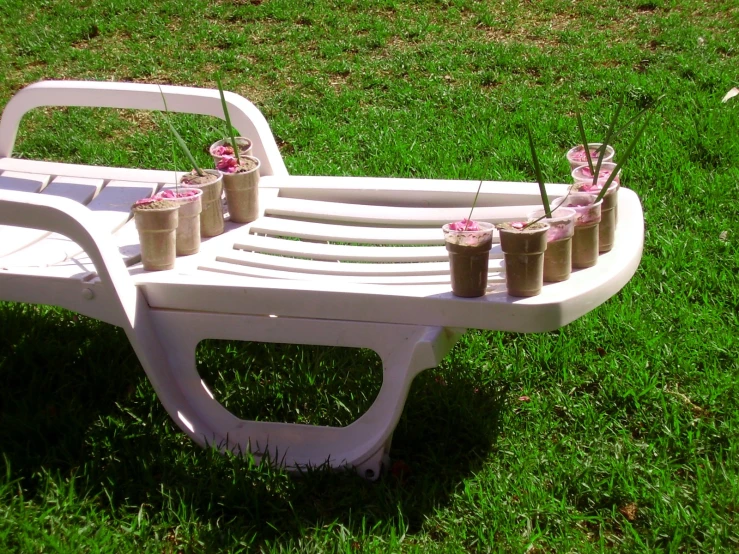 a white wooden bench filled with vases on grass