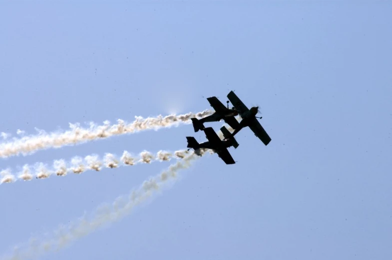 two airplanes flying across a clear sky leaving a trail of smoke