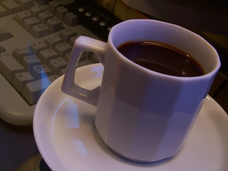 a coffee cup on a saucer next to a computer keyboard