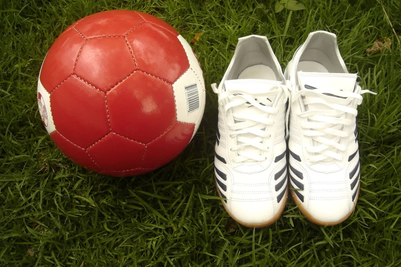 a red and white ball and shoes sitting on green grass
