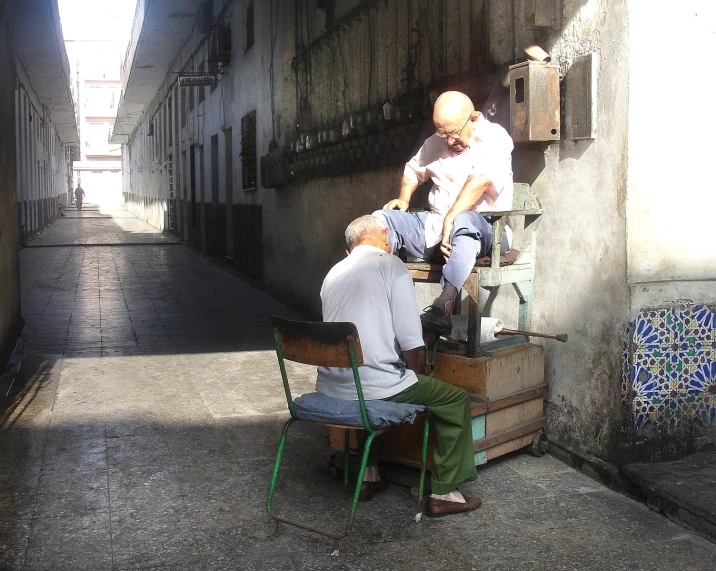 a man sits in a chair as another stands over another man that is sitting down