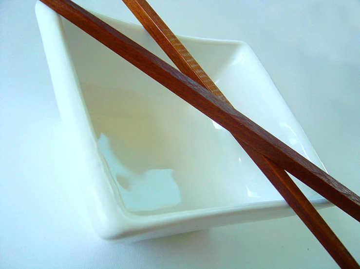 two chopsticks in a square bowl with water on a white table