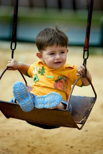 a little boy in a yellow shirt is swinging on a swing