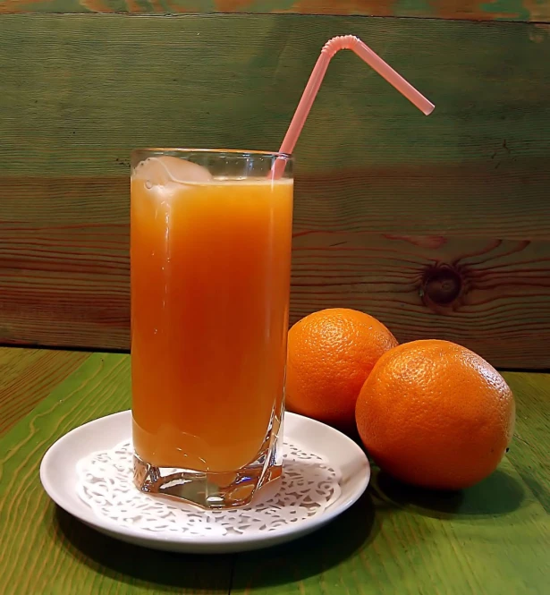 a orange juice is in a glass and beside some oranges