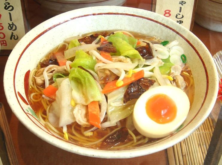 a bowl filled with asian food sitting on top of a wooden table