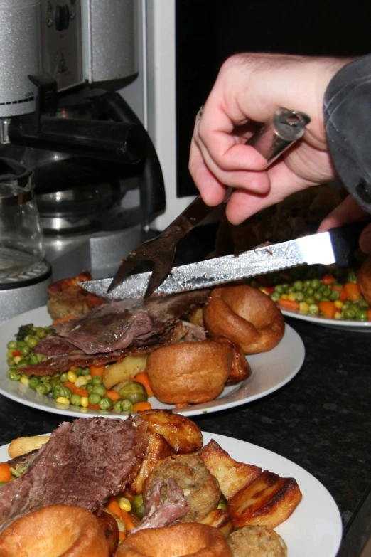 two white plates topped with meat next to vegetables and bread