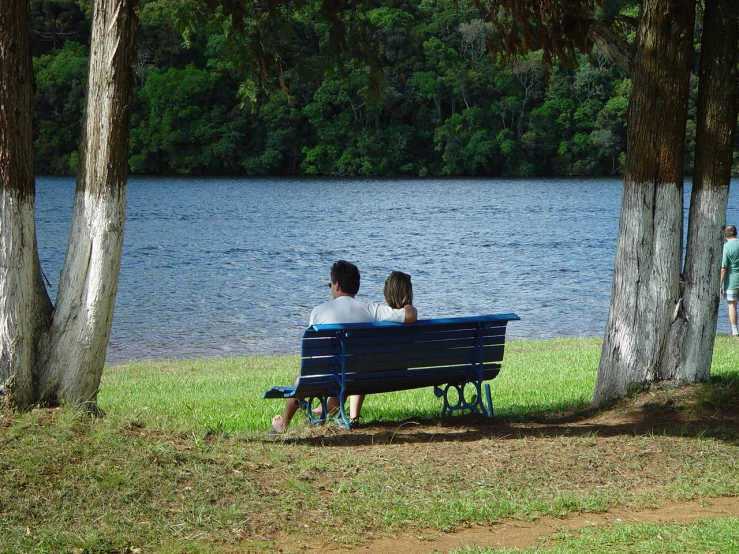 two people sitting on a bench near some water