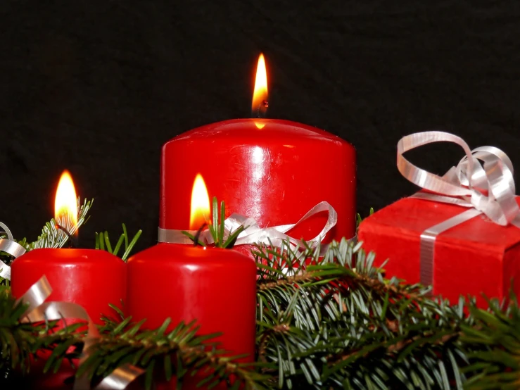 three red candles are sitting beside christmas gifts
