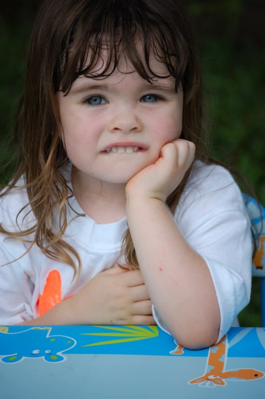 a little girl sitting at a table with her hand on her chin
