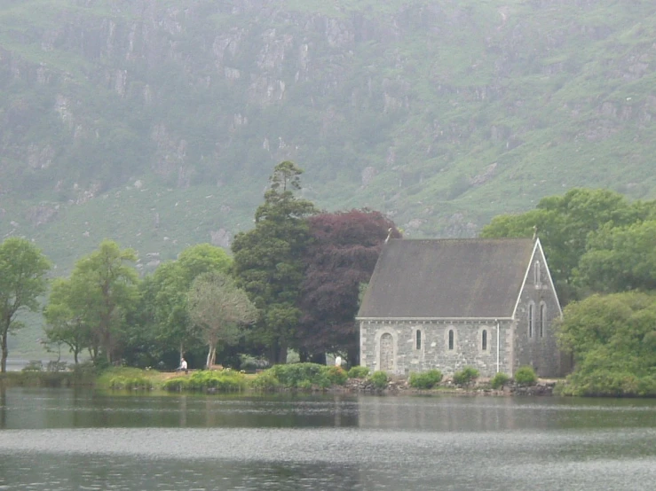 an old church near the water with mountains in the background