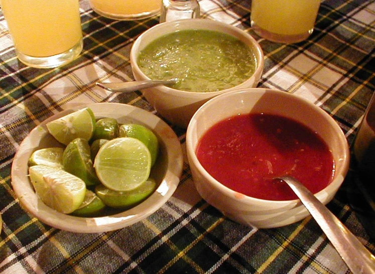 three bowls of food with pickles and green beverages in the background