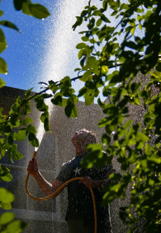 a man wearing a hat holds an open hose next to a large fountain of water