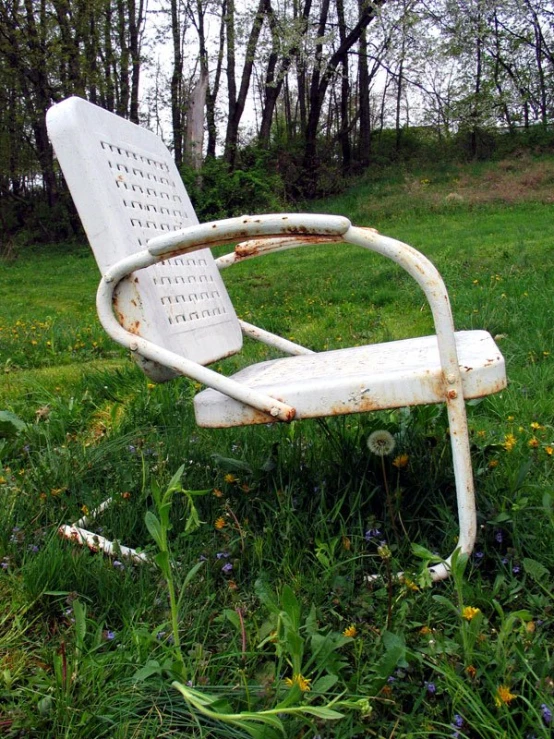 a rusty white park chair in a grassy field